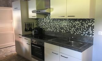 A modern kitchen with white cabinets and a gray countertop. The wall is decorated with an elegant mosaic-like tile pattern.