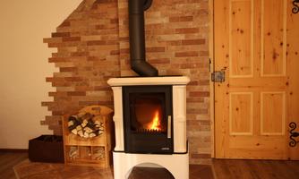 A modern fireplace stands in front of a rustic stone wall. Next to it lies a wooden box with blankets in the room.