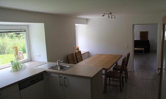A modern kitchen with a large table and wooden chairs.  
Plenty of natural light streams through the windows, creating an inviting atmosphere.