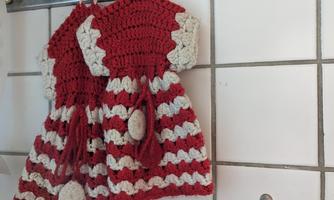 A couple of hand-crocheted dish towels in red and white are hanging on a wall. Next to them is a small decorative wall decoration.