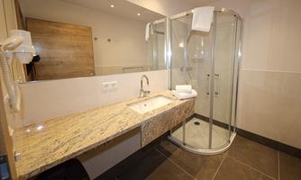 A modern bathroom with a shower and a sink made of granite. The walls are light and there is plenty of light.