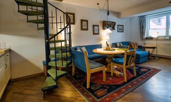 A cozy living kitchen with a spiral staircase and a round table. The room features blue sofas and a beautiful rug.