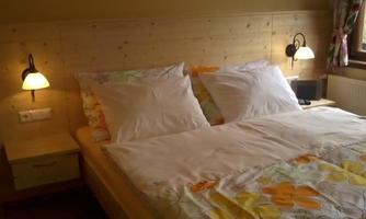 A cozy bedroom with a large bed and bright pillows. On the walls, there are soft lamps and a window treatment with floral patterns.