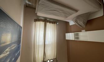 A simple bedroom with a single bed and a large window. The walls are painted in warm colors and there is a view of a water feature.