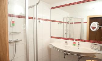 A modern bathroom with a shower and bright tiles. The mirror and the fixtures are simple and functional.