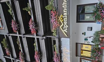 A charming building with many blooming plants on the balcony. The sign displays the name of the aparthotel "Alpenlandhof".
