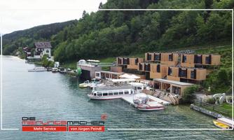 A picturesque harbor with modern wooden houses and a boat dock by the clear water. The surroundings are green and surrounded by hills.