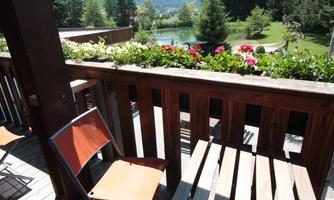 A balcony with a view of a beautiful garden. There are flowering plants and comfortable chairs to relax.