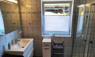 A modern bathroom with tiled walls and a large shower cabin. There is a bathtub, a sink, and a small cupboard for storage.