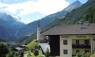 A picturesque valley with a beautiful inn and a church in the background. The surrounding mountains are covered with green forests and snow-capped peaks.