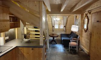 A cozy room with a modern kitchen and a seating area. The wooden walls and floor give a rustic atmosphere.