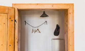 An inviting entrance area with a wood-look door and a wall clock. There are coat hangers hanging in the room and a lamp is mounted over the area.
