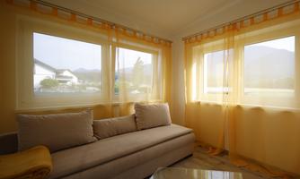 A bright room with a beige sofa and large windows. The curtains are yellow and let in a lot of sunlight.