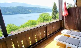 A sunny terrace with loungers and a view of an idyllic lake. In the background, gentle hills and trees can be seen.
