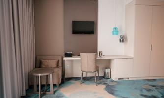 A modern room with a table, a chair, and a seating area. A television is mounted on the wall, and the decoration is in soft colors.