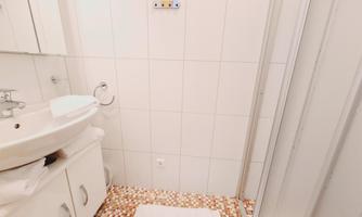 A small bathroom with bright tiles and a sink. There is a shower and a white towel floor.