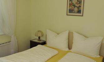 A cozy bedroom with a double bed and yellow bedding. The walls are painted in soft shades of yellow, and a bright light shines from the ceiling.