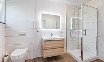 A modern bathroom with a shower cabin and a sink under a illuminated mirror. The walls are in bright tiles and the floor is made of wood.