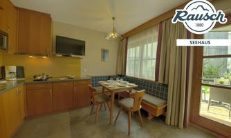 A modern kitchen with wooden cabinets and a small dining table. Well-lit with a large window and a cozy atmosphere.