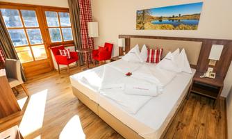 A cozy hotel room with a large bed and decorative pillows. The decor is modern and well-lit, with a beautiful view from the windows.