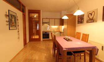 A modern kitchen with a large dining table and wooden chairs. The space is bright and friendly designed.