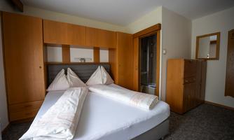A cozy bedroom with a double bed and wooden cabinets. There is a window and a small area with a mirror.
