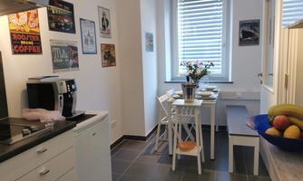 A modern kitchen with a dining area. The table is nicely decorated and there are fresh fruits in a bowl.