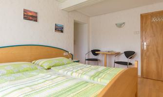 A cozy room with a double bed and green-striped bedding. Pictures hang on the wall, and there is a small table with chairs.