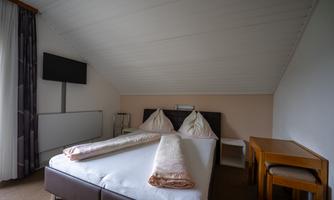 A cozy bedroom with a double bed and two pillows. There is a table and a television on the wall.