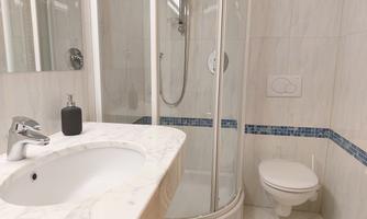 A modern bathroom with a shower and a marble sink. The walls are designed with light tiles and blue accents.