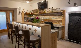 A modern bar with a wooden counter and white walls. In the background, alcoholic drinks and glasses are on shelves.