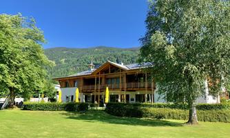 A modern building amidst green meadows and trees. In the background, gentle hills are visible under a clear blue sky.