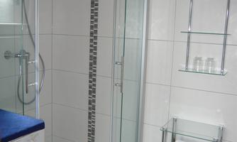 A modern bathroom with a clear shower niche and white tiles. Towels and toiletries are neatly stacked.