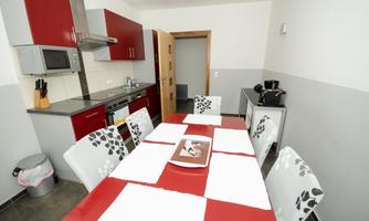 A modern kitchen with red cabinets and a large dining area. The table is set and there is a view of the open door.