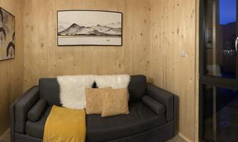 A cozy living space with wood paneling and a gray sofa. Artworks hang on the wall, and the evening ambiance is visible through the window.