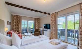 A comfortable hotel room with two beds, a television, and a cozy armchair. Large windows offer a view of the surroundings.