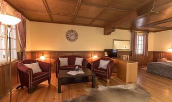 A cozy living room with red armchairs and a wooden table. The walls are made of wood, and there are large windows that provide plenty of light.