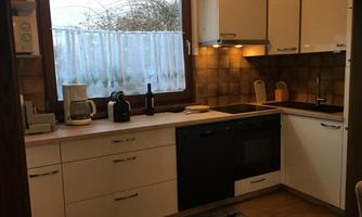A modern kitchen with white furniture and a black stove. The window lets in a lot of daylight.