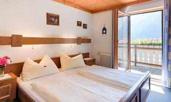 A cozy bedroom with two beds and wooden paneling. Large windows provide a view of the mountains and plenty of daylight.