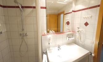A modern bathroom with a shower and towel radiator. Bright tiles and a large mirror create a friendly atmosphere.