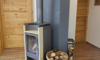 A modern wood stove stands in a bright room with wooden paneling. Next to the stove is a basket with logs.