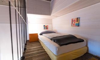 A modern bedroom with a single bed, minimalist decor, and hardwood floor. Two colorful pictures are hanging on the wall.