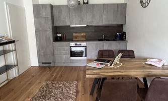 A modern kitchen with a dining table and chairs. The floor is made of wood and there is a rug in front of the table.