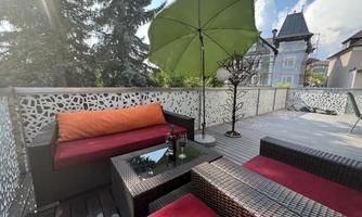 A modern terrace with rattan furniture and colorful cushions. A large sun umbrella provides shade and a relaxed atmosphere.