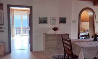 A cozy room with a table and chairs. In the background, there is a hallway and a view outside.