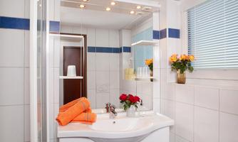 A modern bathroom with a white sink and large mirrors. Fresh flowers and colored towels create an inviting atmosphere.