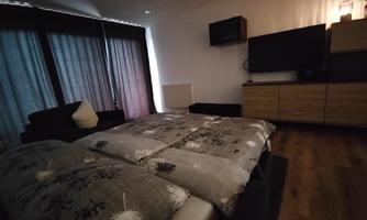A cozy bedroom with a large bed and a TV. The windows are covered with curtains, and the room has a modern look.