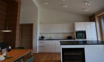 Modern kitchen space with white kitchen furniture and a large window. A wooden table is decorated with wine and glasses.