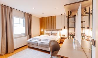 A modern bedroom with a comfortable bed and simple design. There is a desk with a chair and decorative lighting.