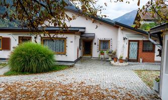 A beautiful house with a paved front yard. The ground is covered with autumn leaves and mountains can be seen in the background.